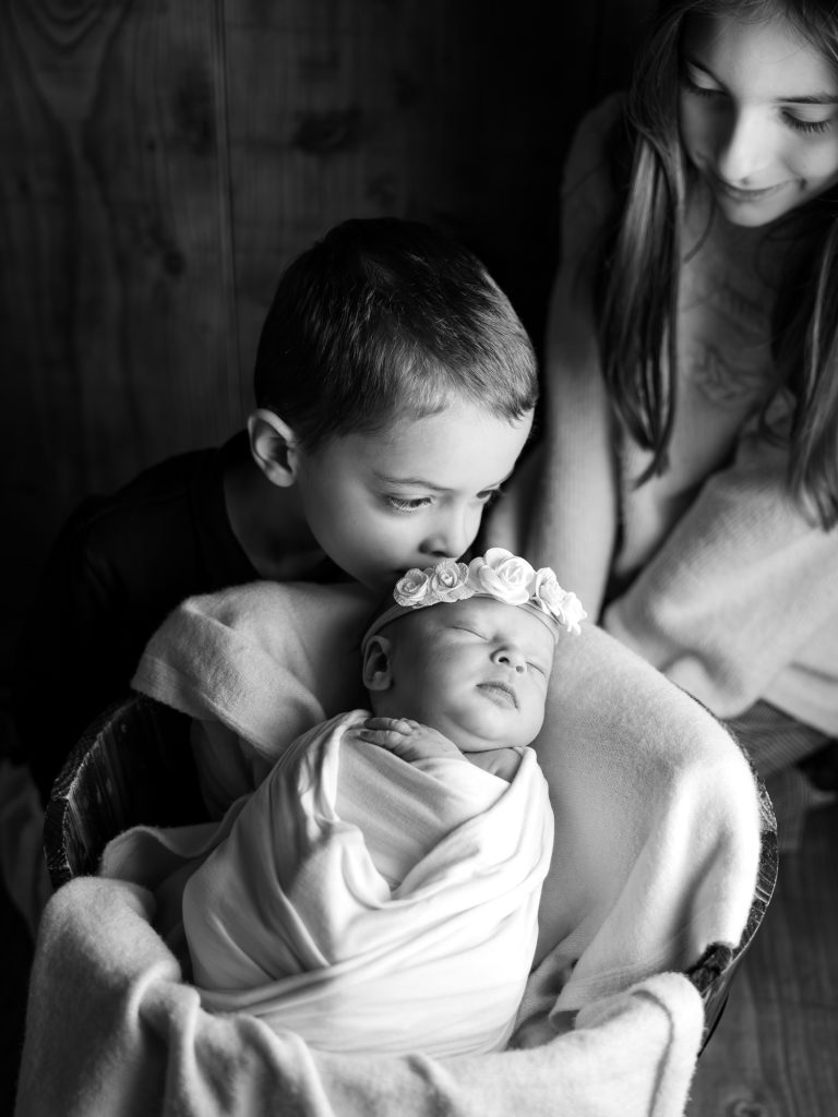 un grand frère qui fait un bisou sur la tête de s petite soeur en séance photo naissance au studio de Audrey LE BIHAN PHOTOGRAPHIES à Plougastel daoulas en Bretagne